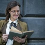 Happy adult woman reading book with interest on street