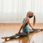 Full body of slim female in sportswear practicing yoga exercises in front split while training in light room on wooden floor