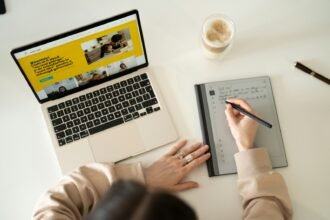 a person is writing on a notebook while using a laptop