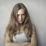 Portrait of a fierce woman with crossed arms and intense expression on a gray background.