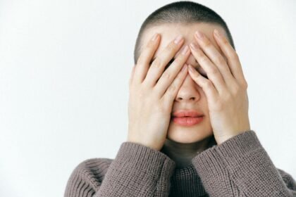 A woman with a neutral expression covers her face with her hands, conveying a sense of introspection.