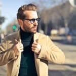 Fashionable young man with sunglasses poses outdoors in a sunny Budapest street scene.