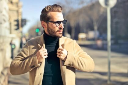 Fashionable young man with sunglasses poses outdoors in a sunny Budapest street scene.